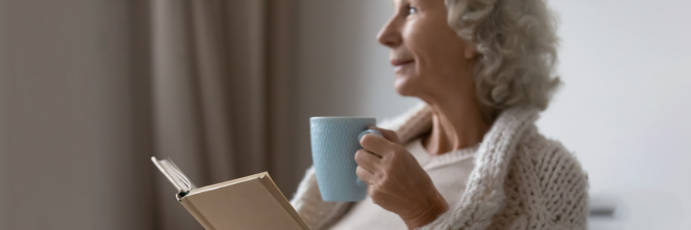 donna anziana che beve un tè mentre legge un libro