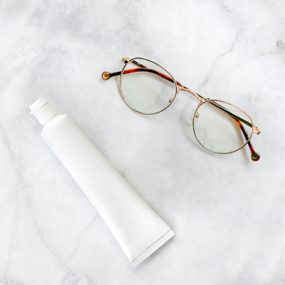 white tube of toothpaste and wire frame glasses on neutral background